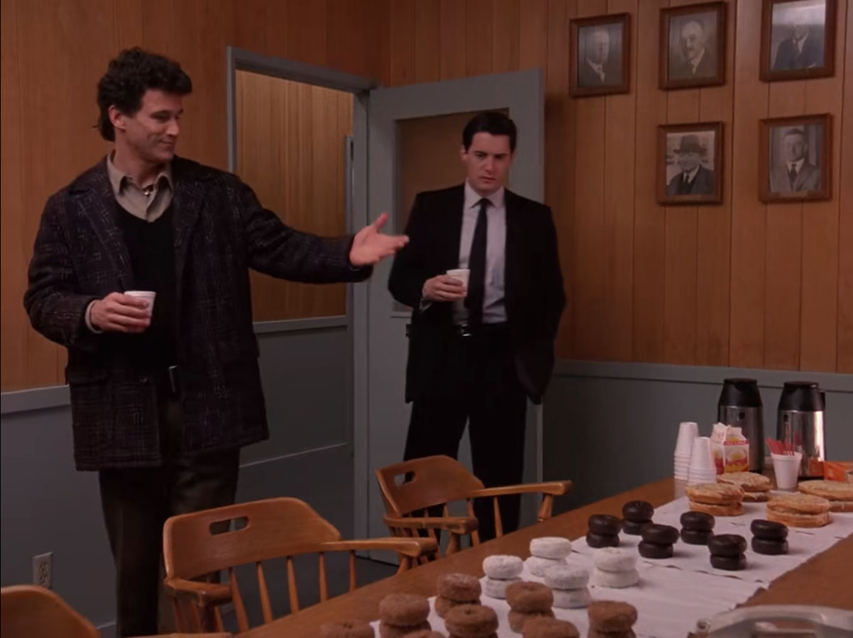Sheriff Truman and Agent Dale Cooper enter a conference room with a table of doughnuts