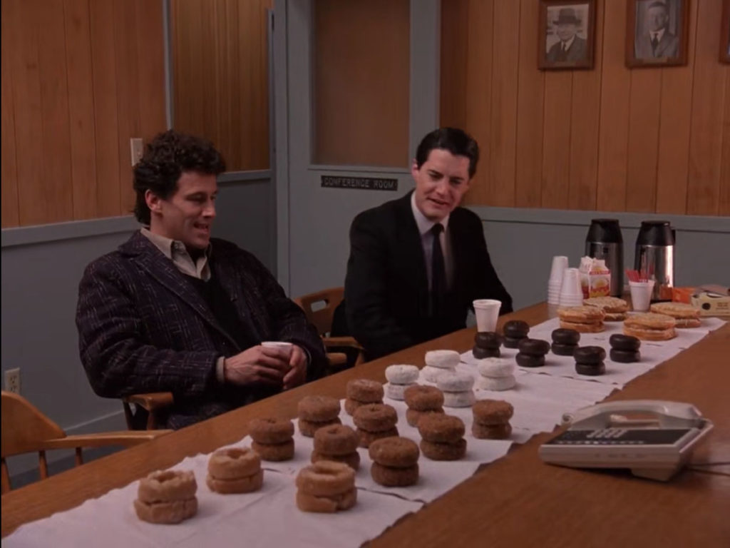 Sheriff Truman and Agent Cooper seated in a conference room with a table full of doughnuts.