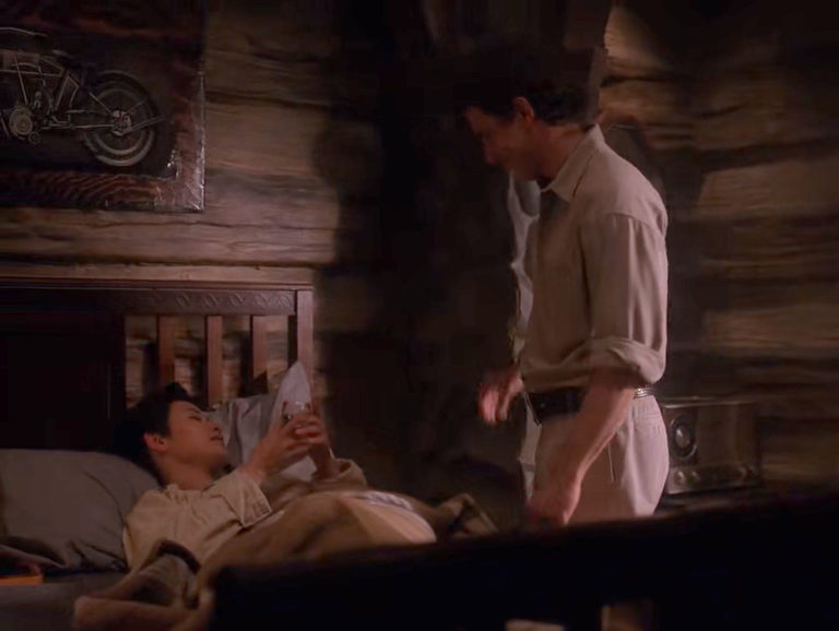 Josie Packard in bed while Harry Truman stands nearby.