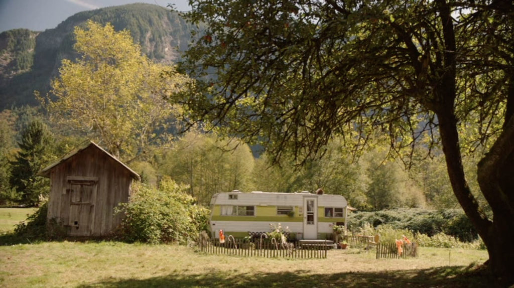 Trailer in a field next to a wooden shack