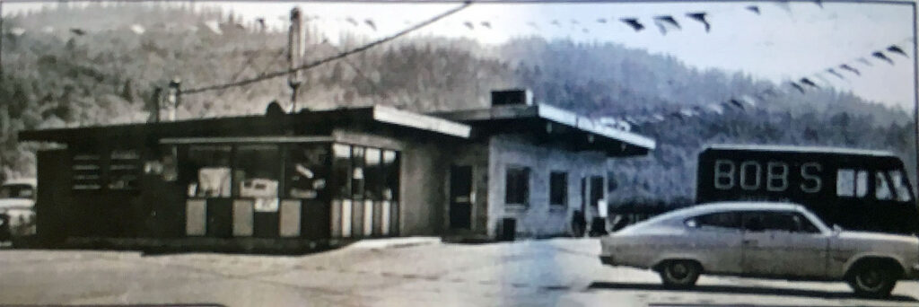 Black and white photo of a restaurant building with a car and truck parked in a parking out.