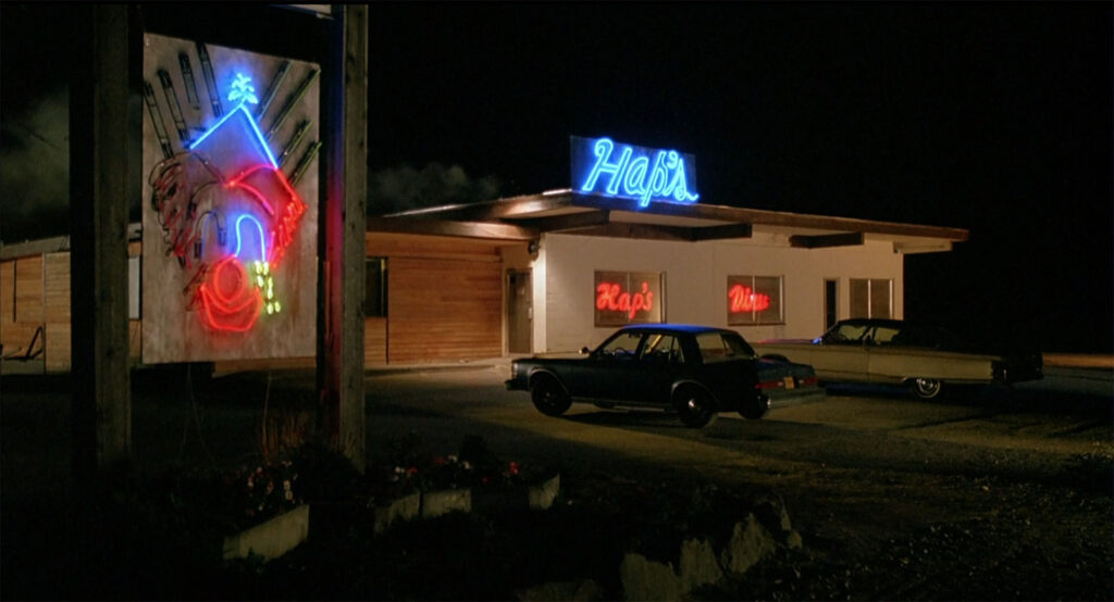 Exterior of a building at night with neon signs and cars in the parking lot.