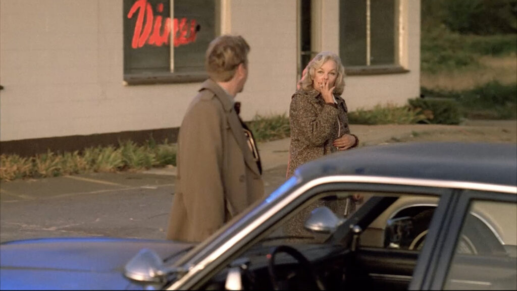 Agent Stanley talks to Irene who is smoking while walking to her car.