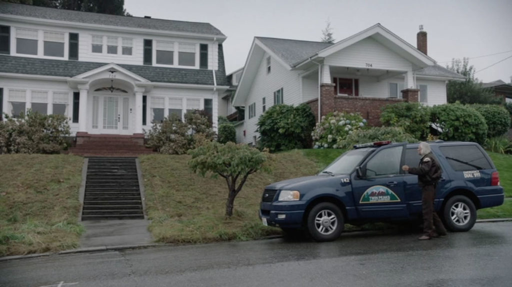 Twin Peaks Sheriff Department vehicle parked on the street in front of a white home sitting on a hill.