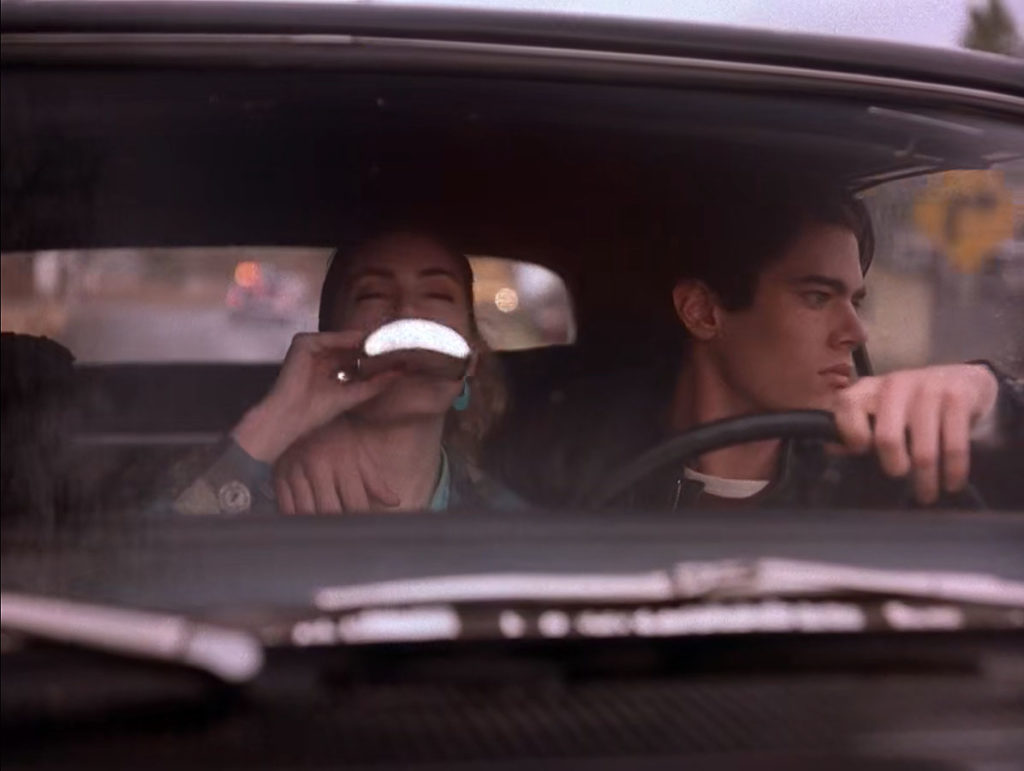 Shelly drinks from a silver flask while Bobby drives his car.