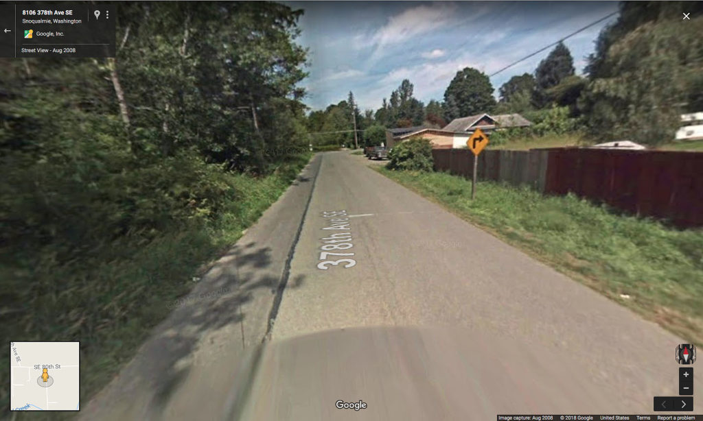Google maps image of a road with a yellow right turn side and a brown fence.
