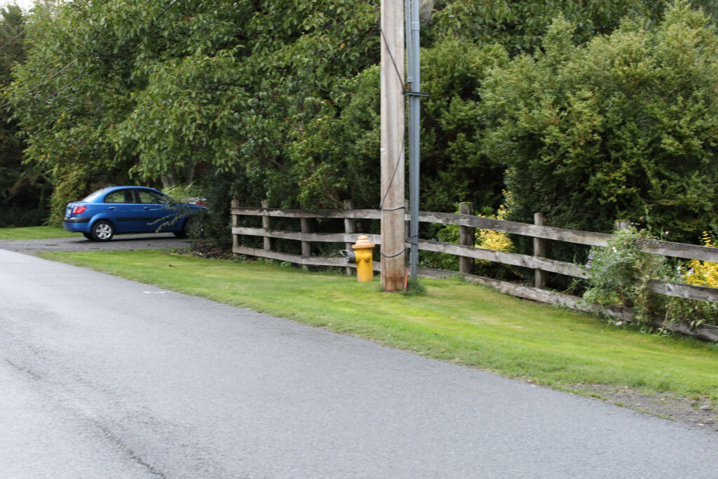 Road with a fence and a utility pole. A blue car is parked in a drive way.