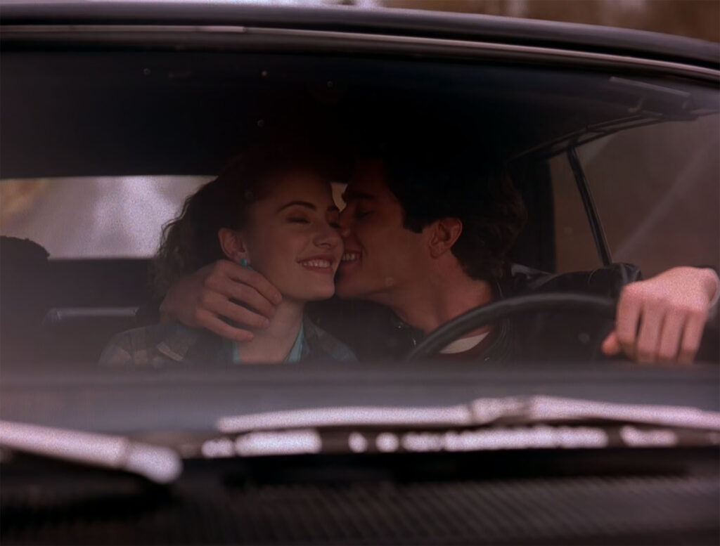 Bobby kisses Shelly on the cheek while he drives his car.