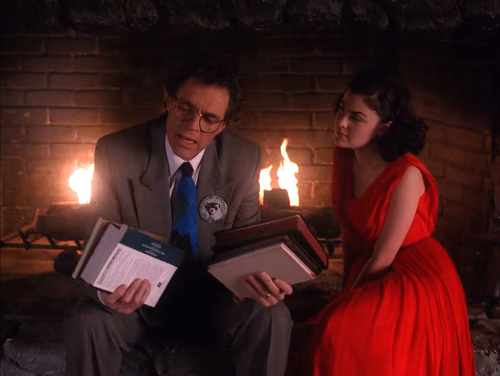 Ben Horne sitting by a fireplace with Audrey holding books