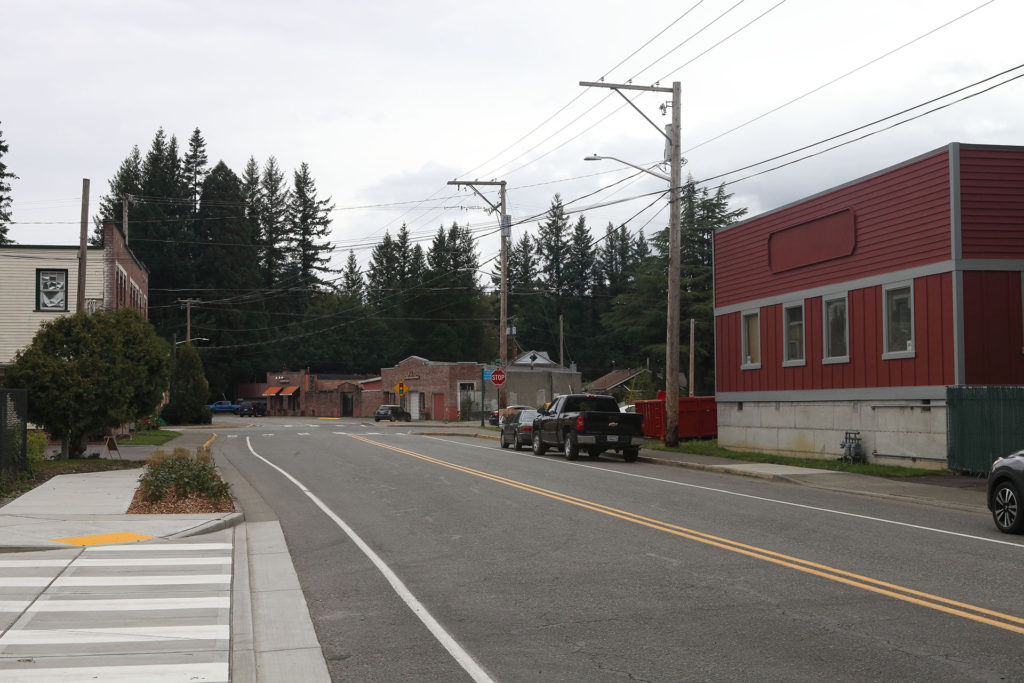 Road lined with buildings and tall fir trees in the distance