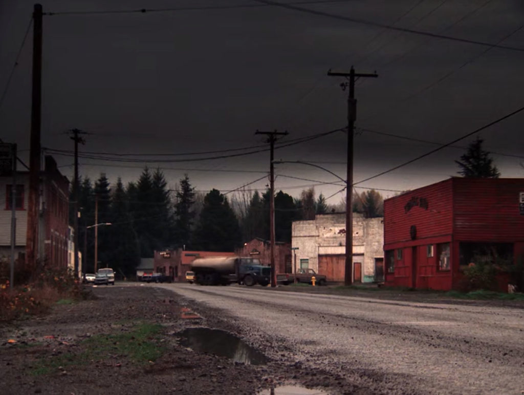 Image from Twin Peaks episode 2010 of wet road lined with buildings and a truck turning onto a side street
