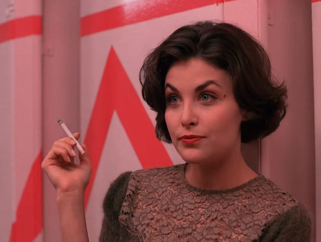 Audrey Horne holding a cigarette in bathroom against striped wall