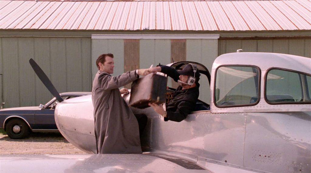 Pilot sitting in a plane handing a suitcase to a person