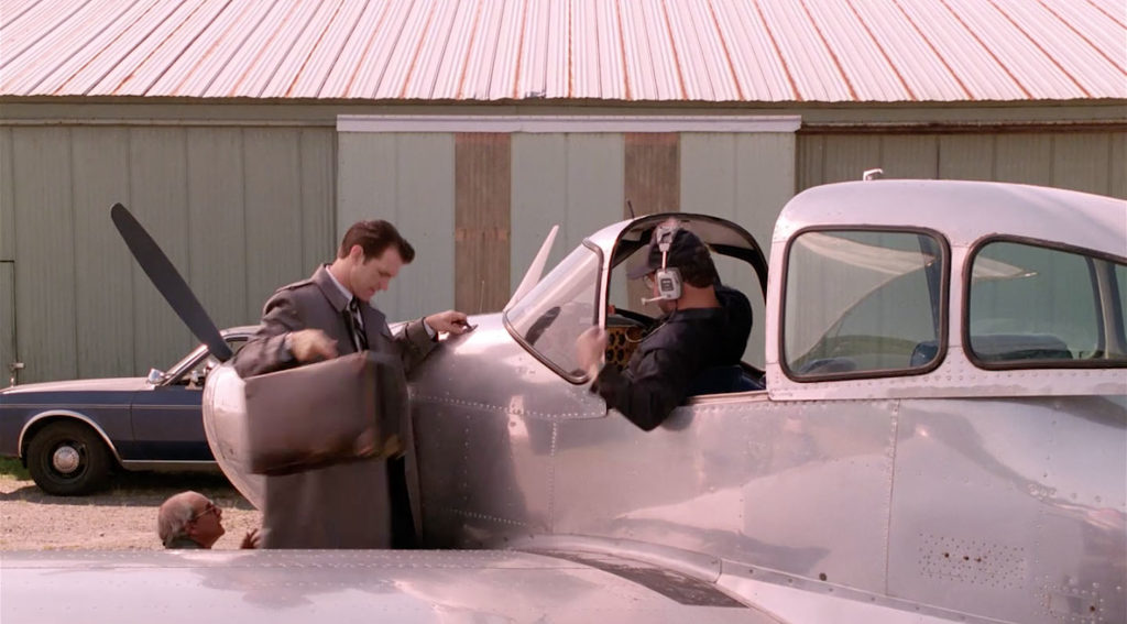 Pilot sitting in a plane handing a suitcase to a person