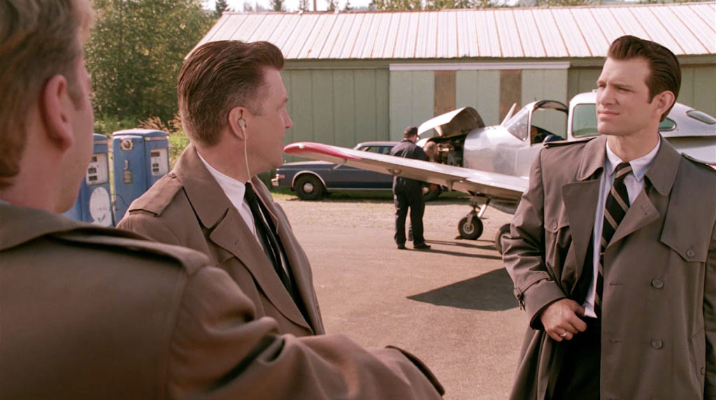 Three people having a conversation by a silver airplane