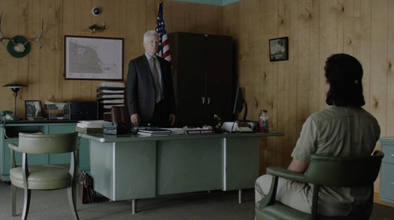 Warden Murphy standing at a desk with Mr. C sitting in a chair