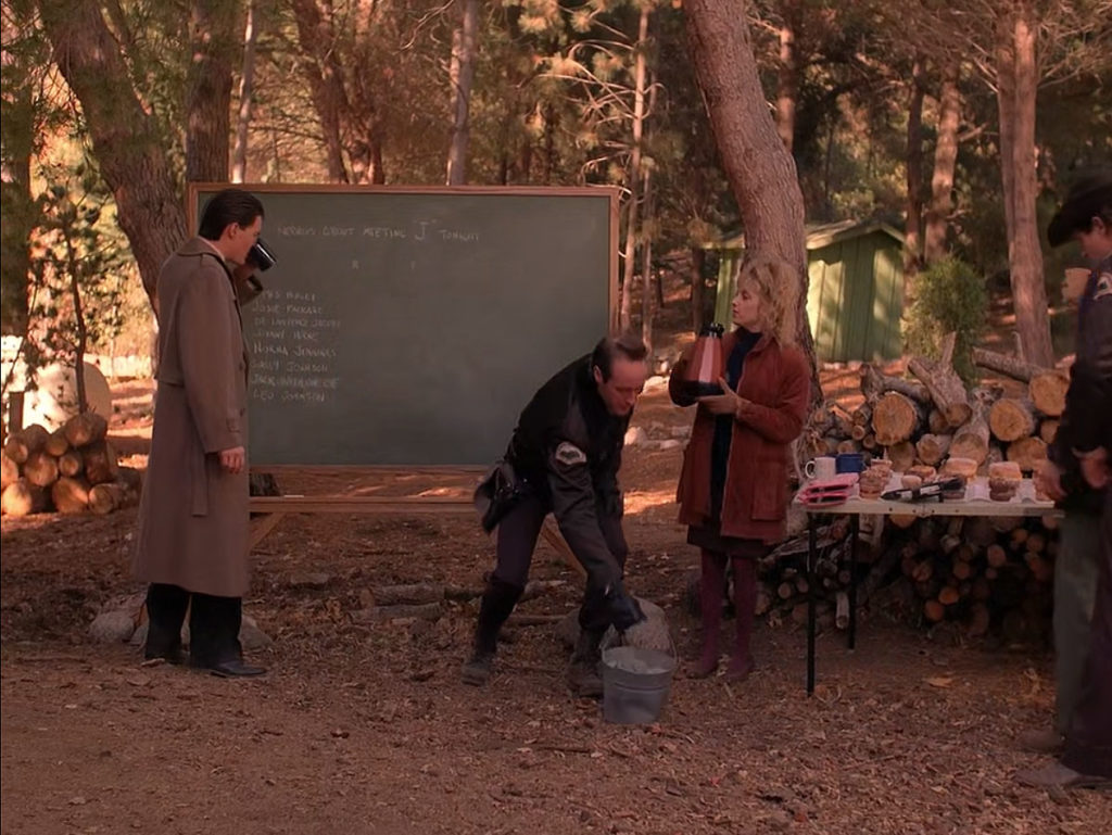 Special Agent Dale Cooper drinking coffee in the woods by a chalkboard