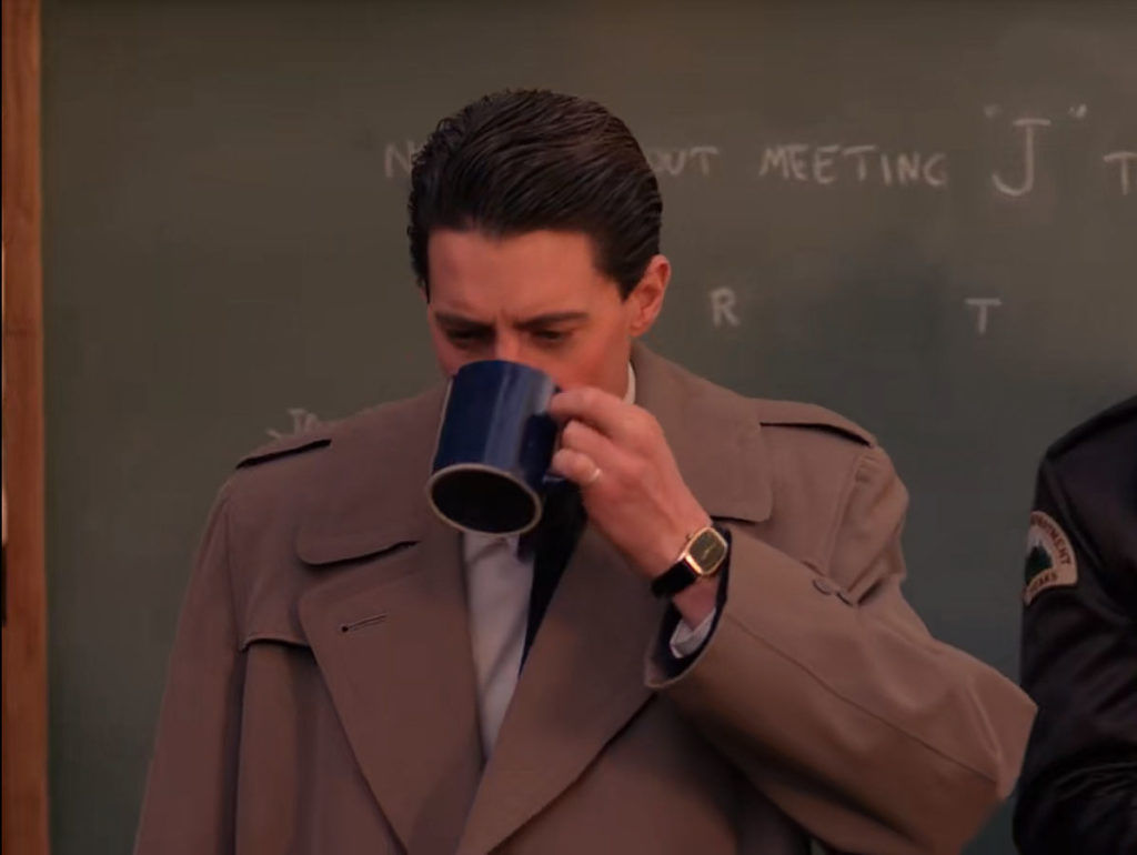 Special Agent Dale Cooper drinking coffee in the woods by a chalkboard