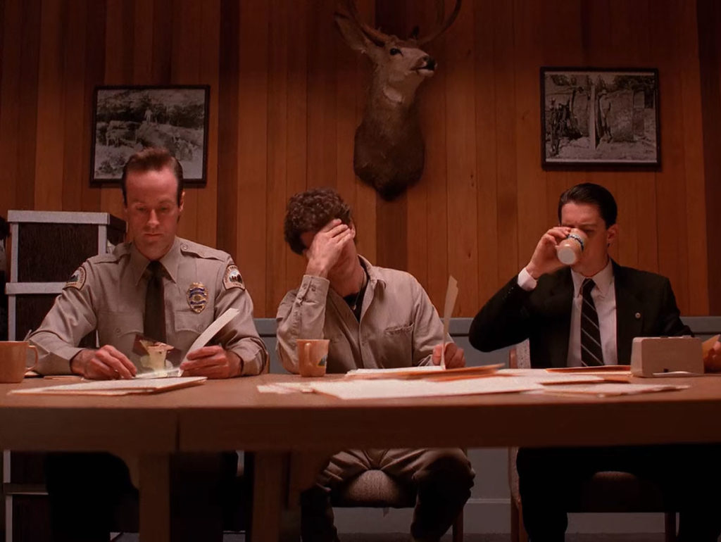 Special Agent Dale Cooper drinking coffee while Deputy Andy Brennan and Sheriff Harry Truman looks at files