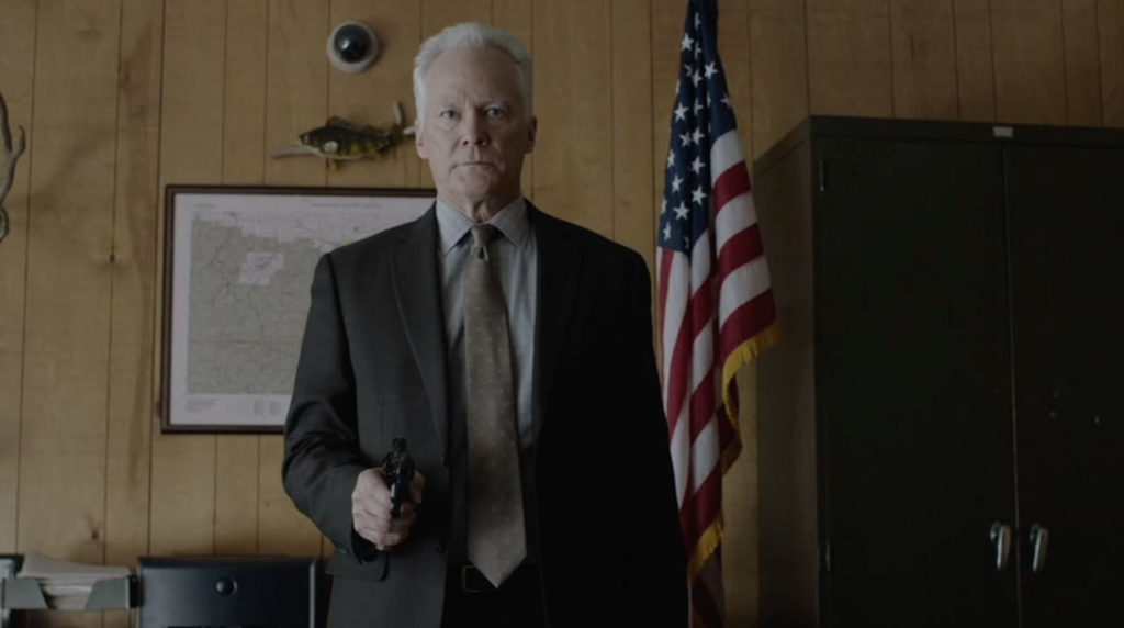 Warden Murphy holding a gun and standing behind his desk