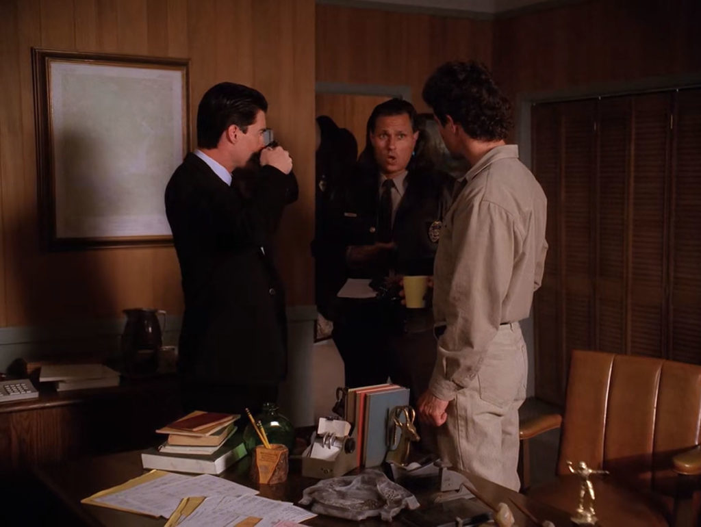 Special Agent Dale Cooper drinking coffee while listening to Sheriff Harry S. Truman and Deputy Hawk in his office