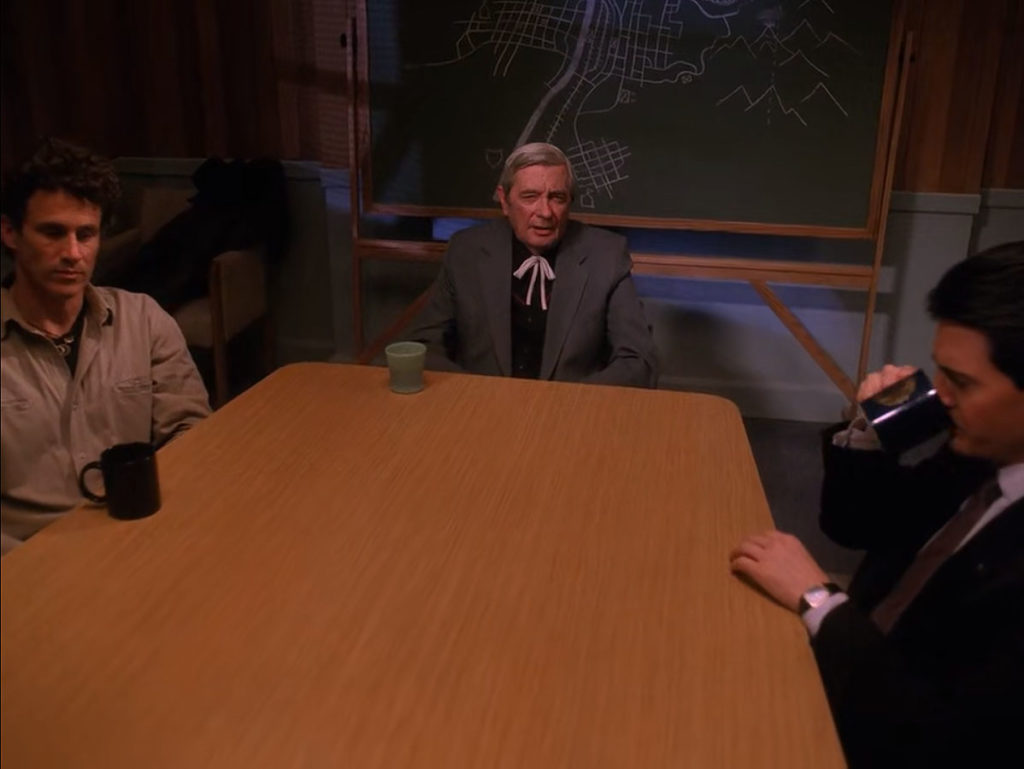 Special Agent Dale Cooper drinking coffee while sitting at a table with Sheriff Truman and Judge Sternwood