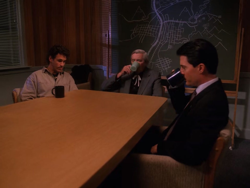 Special Agent Dale Cooper drinking coffee while sitting at a table with Sheriff Truman and Judge Sternwood