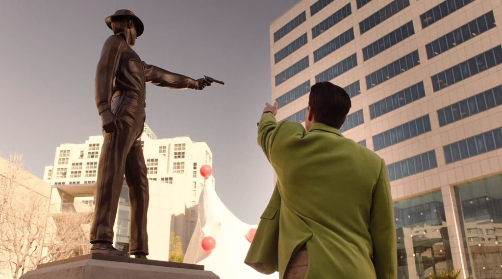 Dougie pointing up to the bronze statue of a guy holding a pistol.