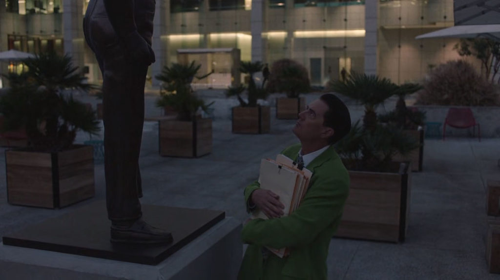Dougie Jones holding files and looking up at bronze statue of man at dusk