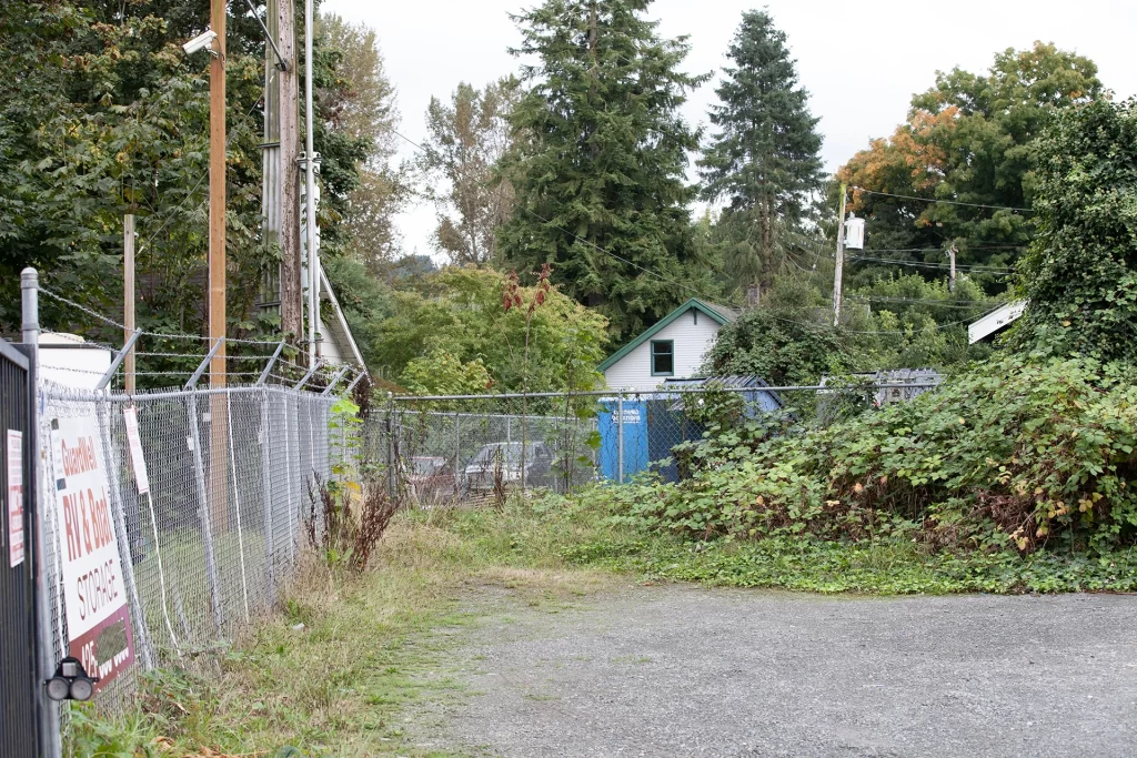 Parking lot with overgrown bushes and a metal fence