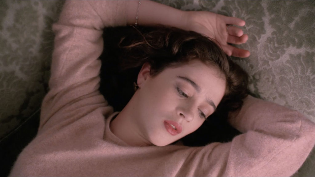 Donna Hayward with arms stretched over her head while laying on the couch