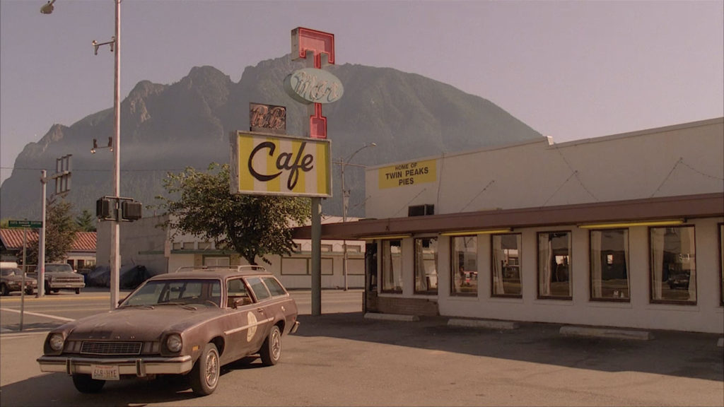 A brown car parked outside Twede's Cafe in North Bend, Washington with Mount Si in the distance.