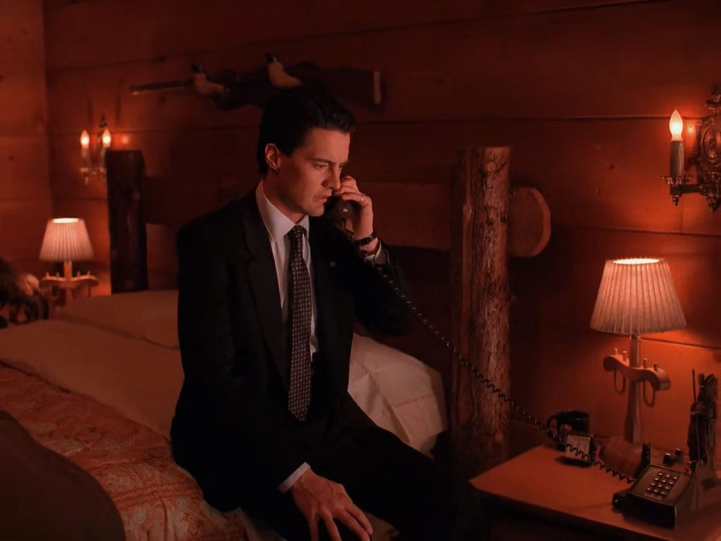 Agent Cooper talking on the phone while sitting on his bed