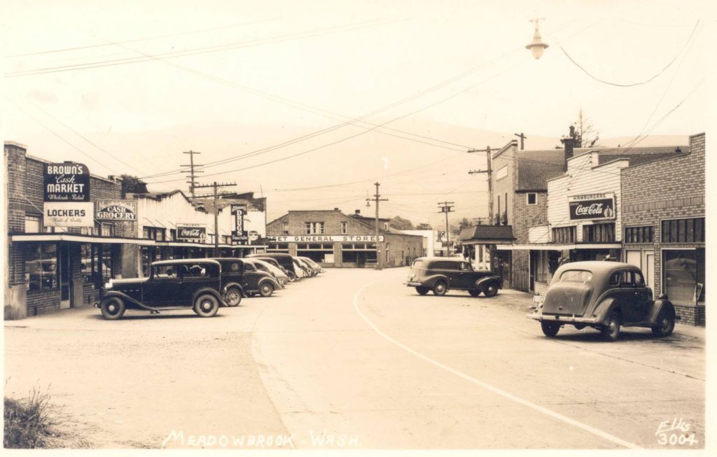 Sepia tone postcard of a town with cars parks along the street