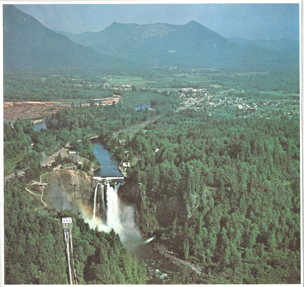 Aerial Photo of Snoqualmie Falls and Snoqualmie Valley. Green covers the land with mountains in the distance