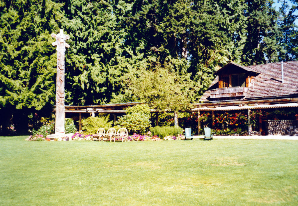 Exterior of wooden lodge with grass and a carved wooden story pole.