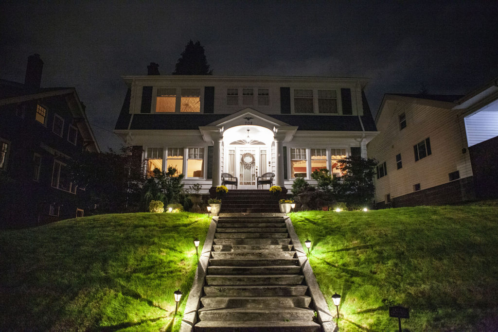 White home sitting on a hill at night with concrete steps leading to the front door flanked by lights