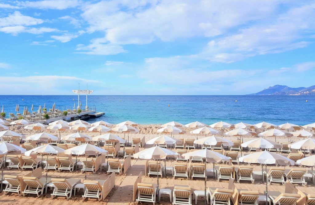 Beach outside Carlton Hotel with rows of beach chairs and umbrellas underneath a cloud-filled, blue sky.