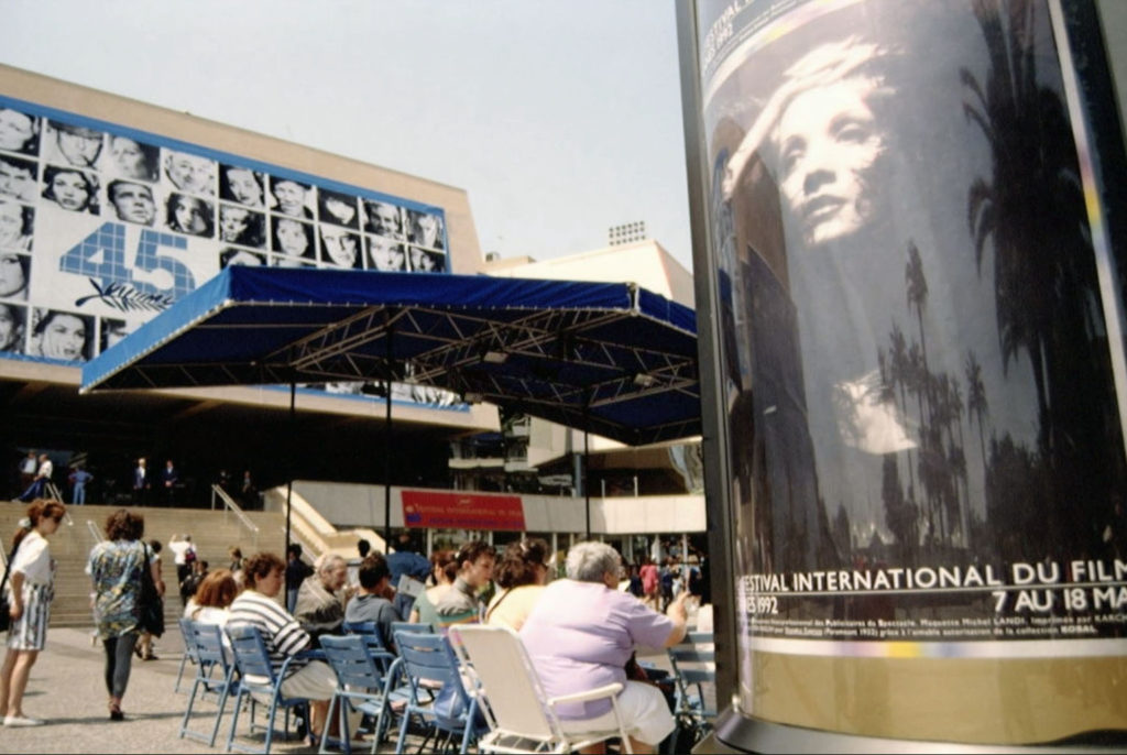 Palais des Festivals et des Congres with people sitting chairs and a movie poster in the foreground.