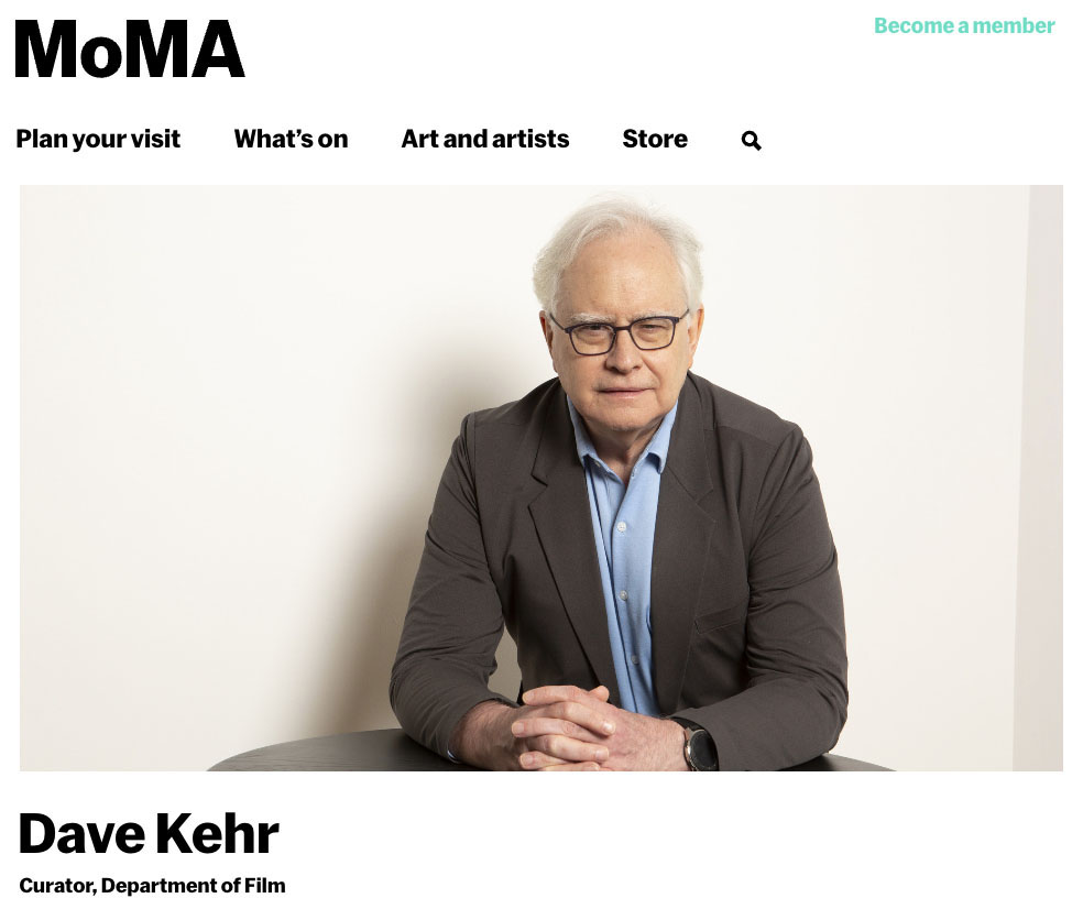 Website image from MOMA.org of Dave Kehr sitting against a cream-colored wall. He is wearing a suit jacket and blue dress shirt while folding his hands.