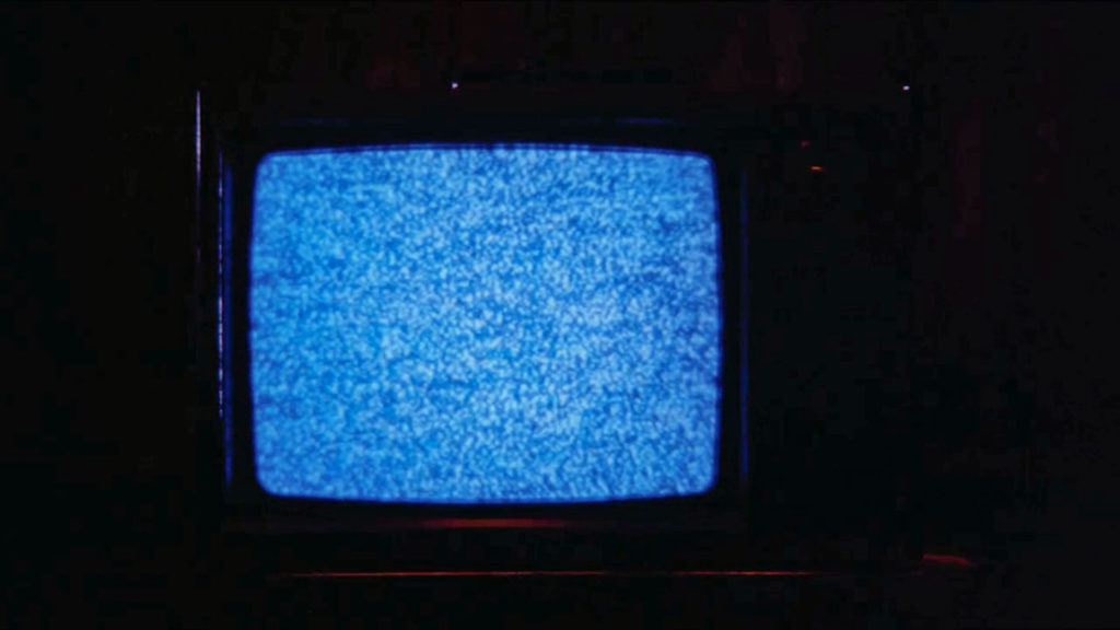 Detail of a television set in shadows with a blue-hued screen filled with snow or static.