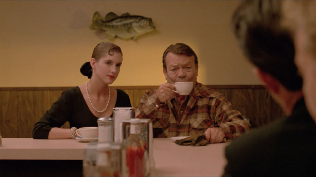 The Old Guy takes a sip of coffee while the French Girl looks at the Special Agents while sitting at Hap's Diner.