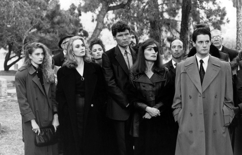 Black and white press image from Twin Peaks, episode 1003 of Laura Palmer's funeral. Shelly Johnson (Madchen Amick), Norma Jennings (Peggy Lipton), Big Ed (Everett McGill), Nadine Hurley (Wendy Robie) and Agent Cooper (Kyle MacLachlan) stand in a line with other townsfolk behind.