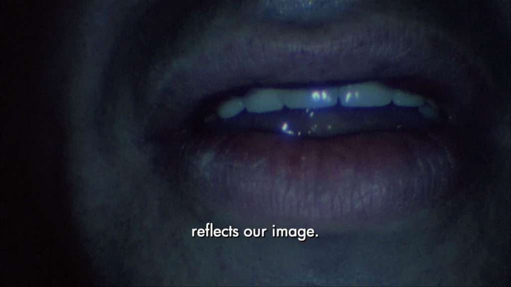 An extreme close-up on a mouth with the word "reflects our image" subtitled
