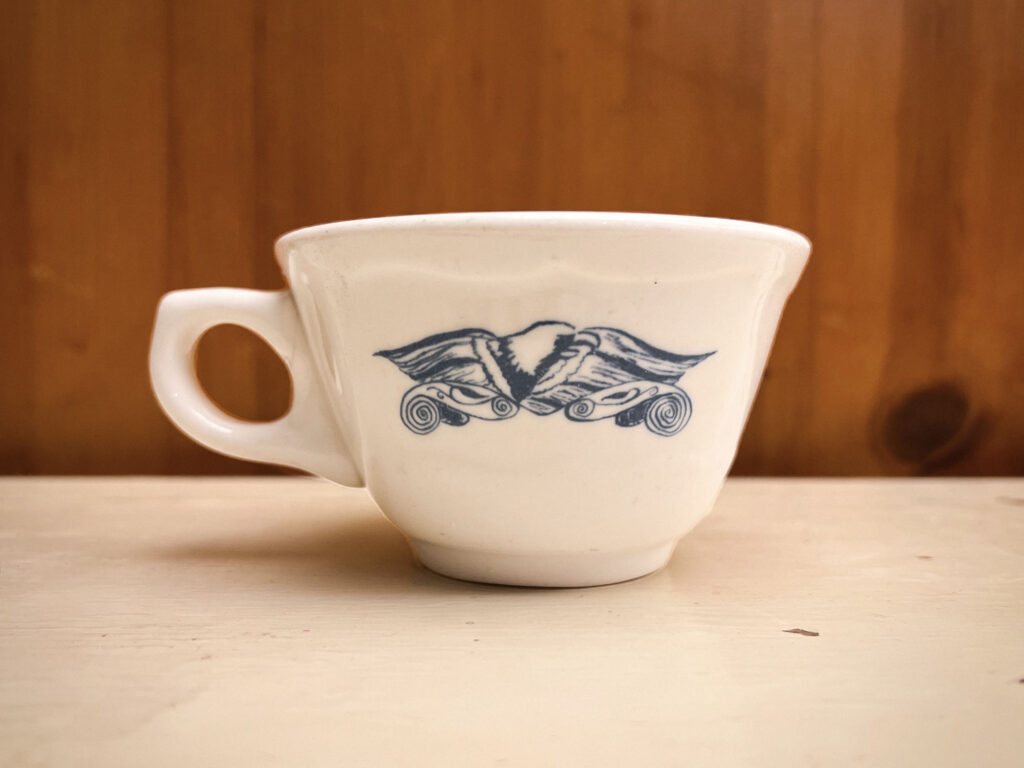 White mug with blue sketch of eagle on a white countertop with wood paneling in the background