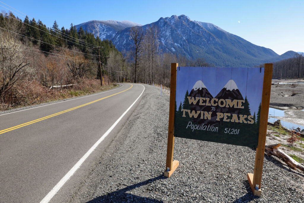Welcome to Twin Peaks sign along Reinig Road in Snoqualmie, WA with Mount Si in the distance.