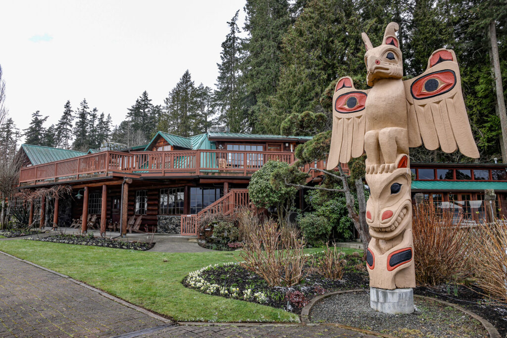 Exterior of Kiana Lodge with tan-colored Thunderbird totem under trees