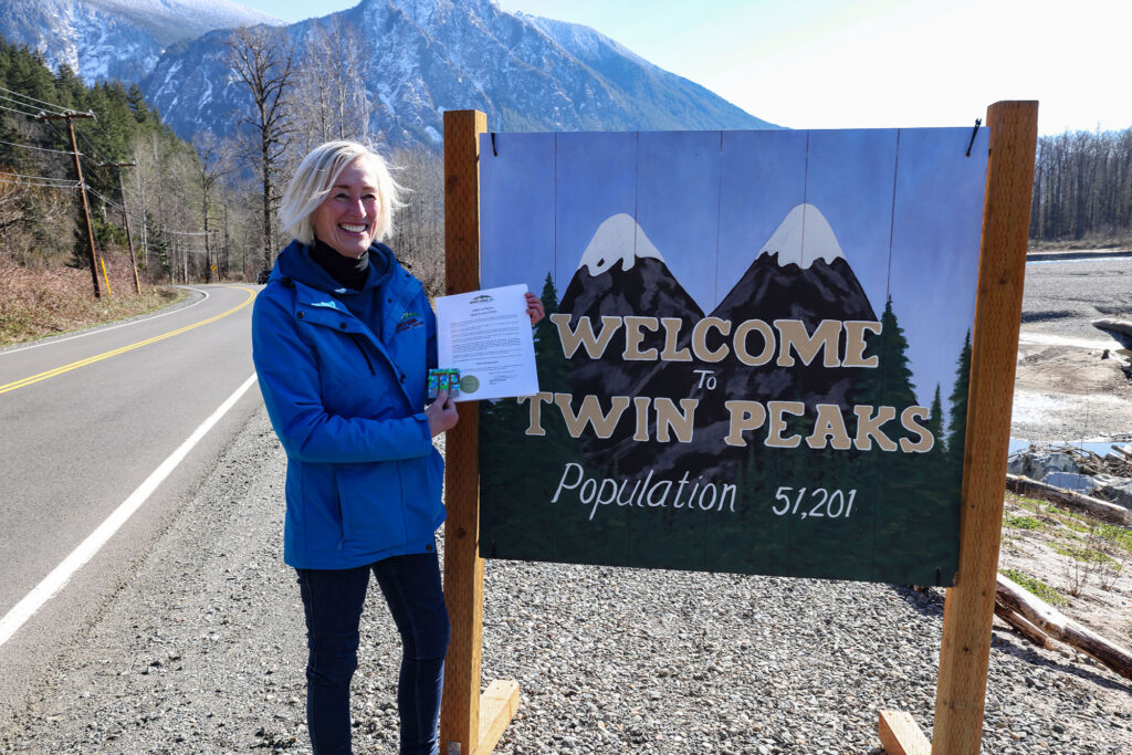 North Bend City Councilwoman Mary Miller holding North Bend proclamation by Welcome to Twin Peaks sign