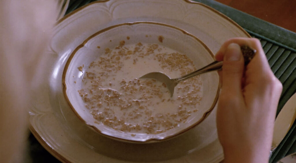 Bowl of soggy cereal with a hand holding a silver spoon against the side of the bowl.