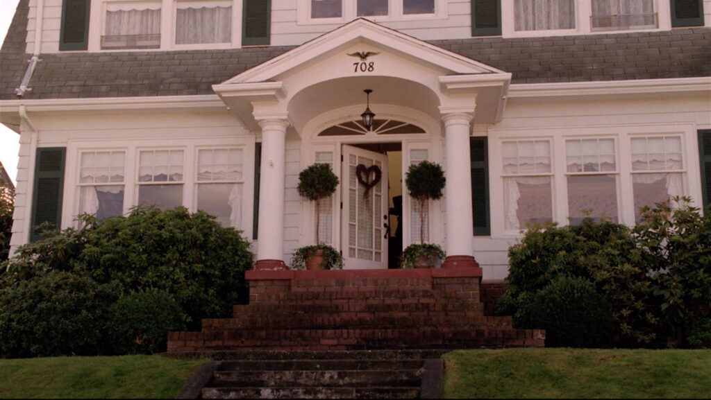 White house on a hill with bushes and Laura Palmer entering the front door.